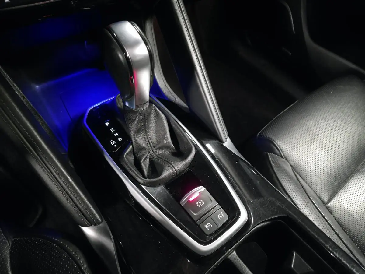 Gros plan sur la console centrale du Renault Koleos bleu, mettant en valeur le levier de vitesse automatique et l'éclairage bleu ambiant.