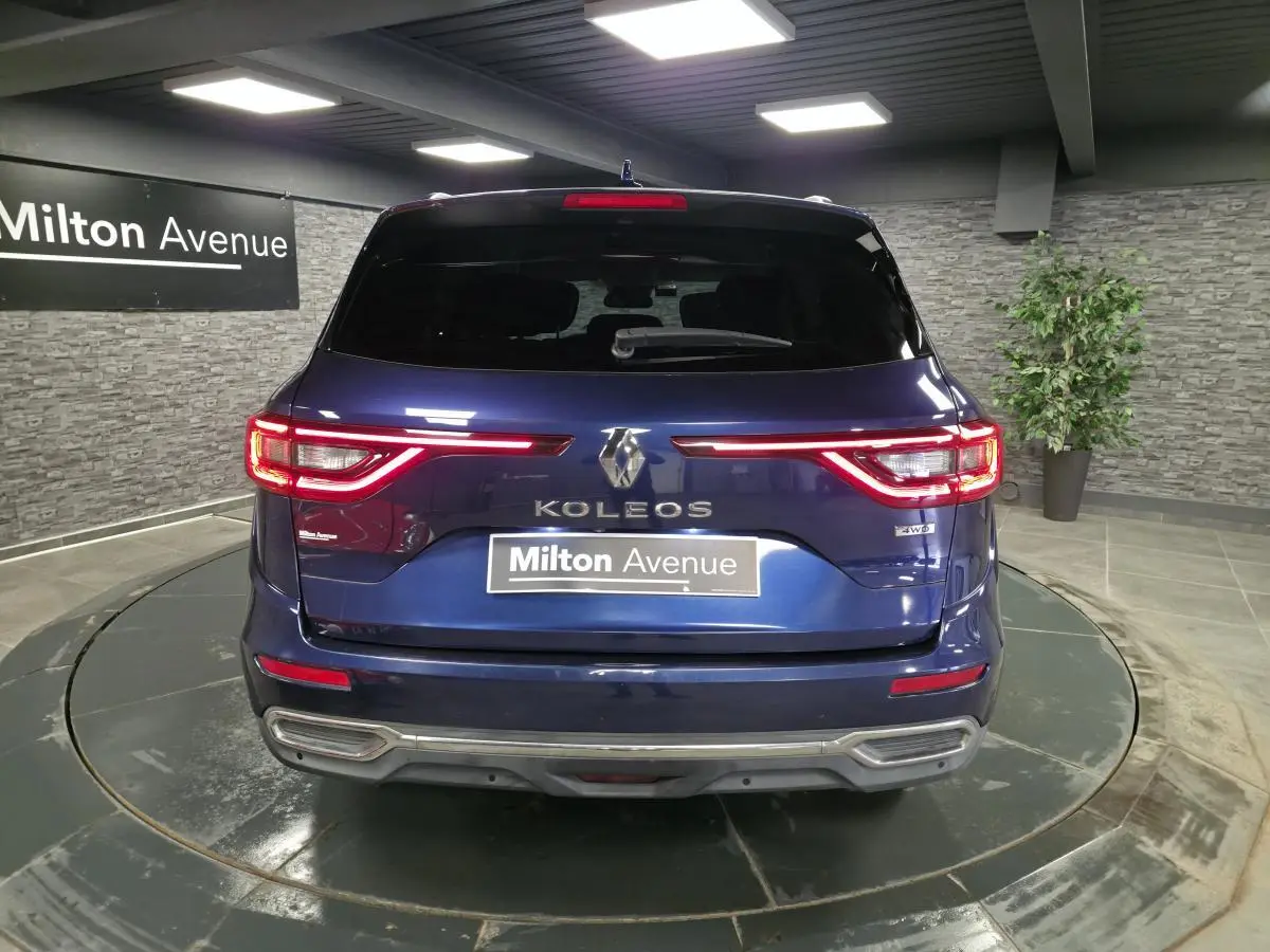 Vue arrière du Renault Koleos bleu de Saxe avec feux LED allumés et logo 4WD visible en intérieur showroom.