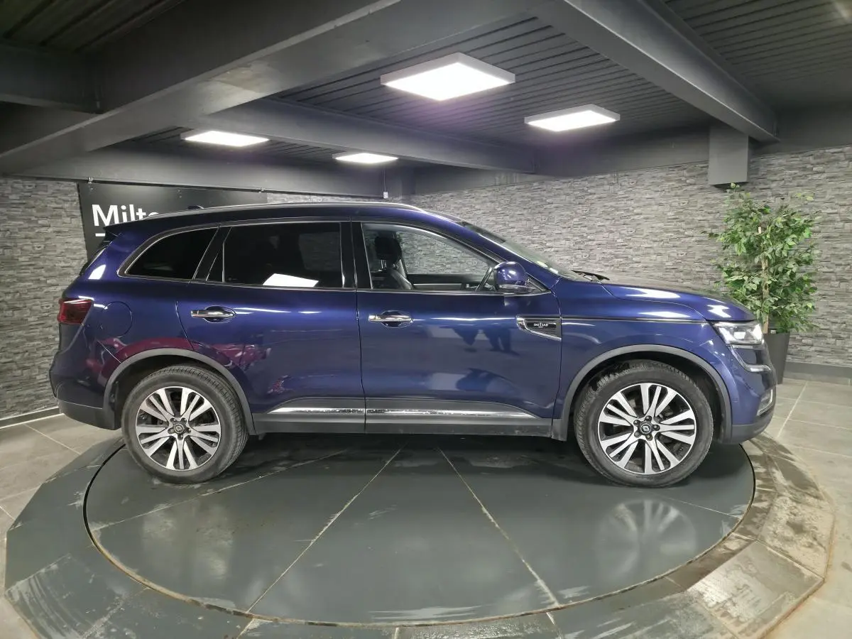 Profil droit du Renault Koleos bleu de Saxe 2017 avec jantes alliage et vitres teintées en intérieur showroom.