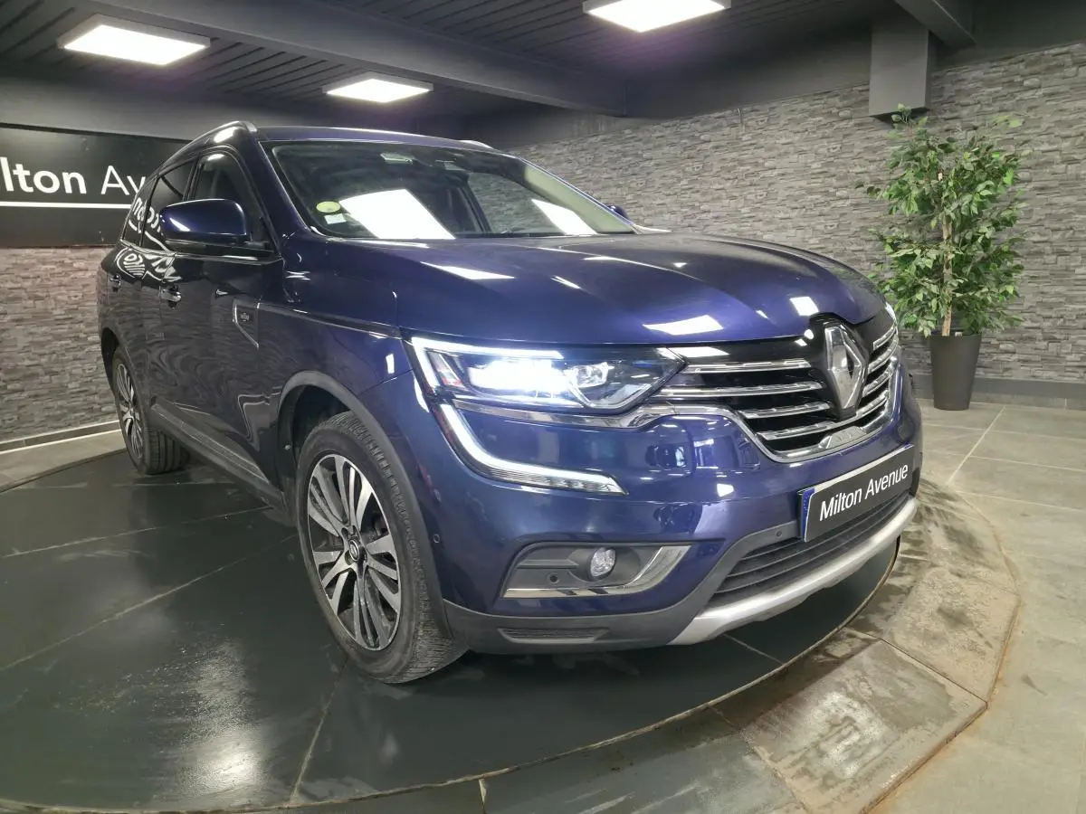 Renault Koleos bleu de Saxe en 3/4 avant droit, feux LED allumés et calandre chromée Initiale Paris visible.