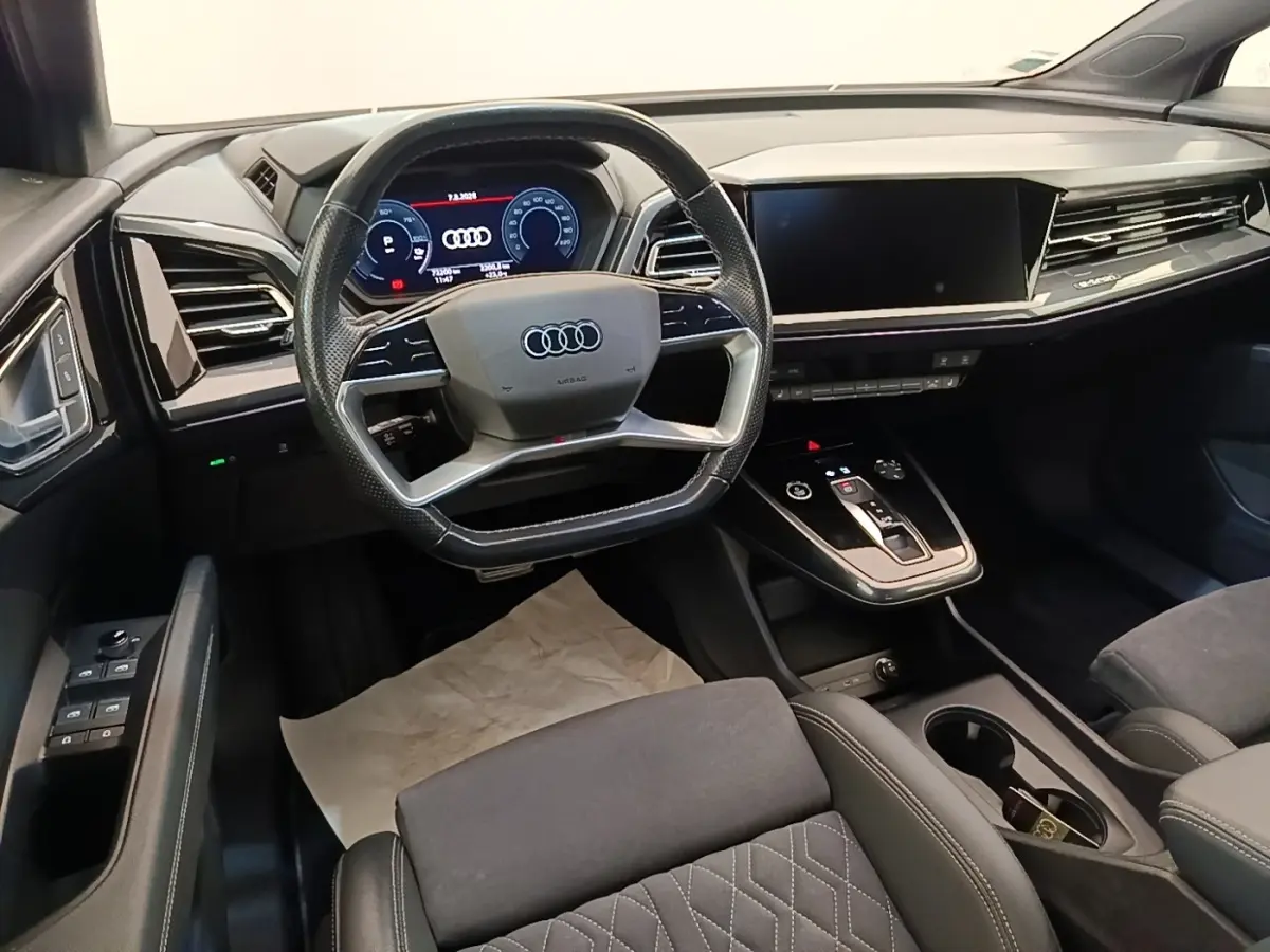 Vue intérieure avant de l'Audi Q4 E-TRON Sportback 2023, tableau de bord noir avec écran tactile et volant multifonctions.
