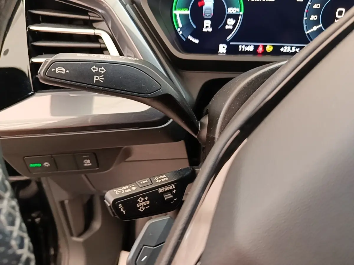 Gros plan sur les commandes au volant côté gauche de l’Audi Q4 E-TRON Sportback noir, avec affichage numérique en arrière-plan.