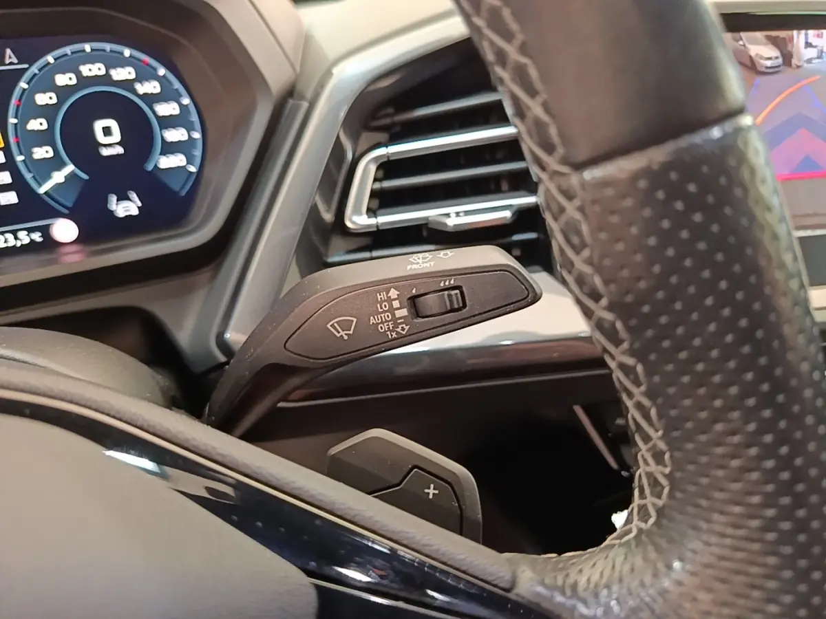 Gros plan sur le volant cuir et levier de commande des essuie-glaces de l'Audi Q4 E-Tron Sportback noir, tableau de bord numérique visible.