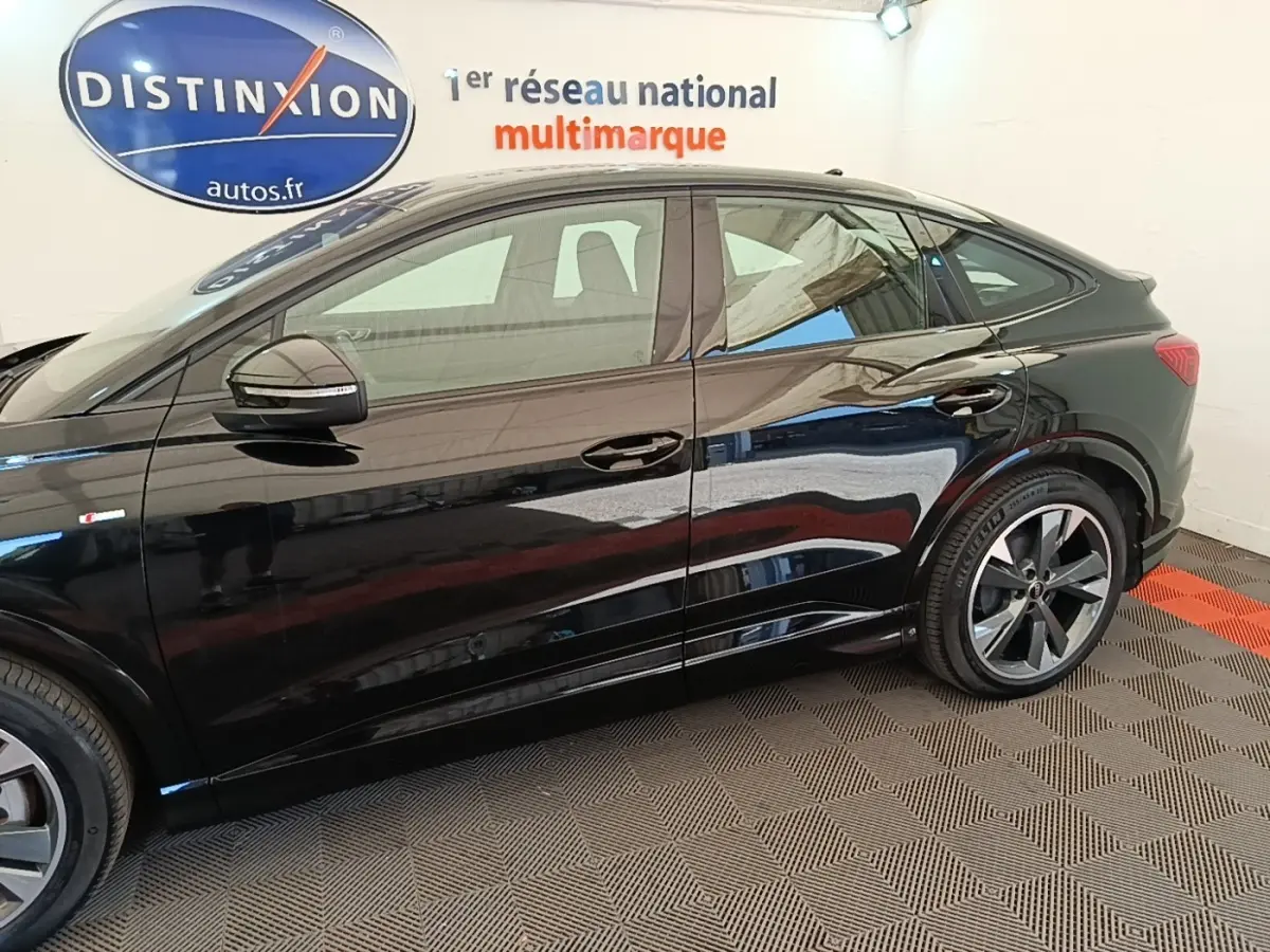 Profil côté gauche d'un Audi Q4 E-TRON Sportback noir 2023, mettant en valeur ses lignes fluides et ses jantes distinctives.