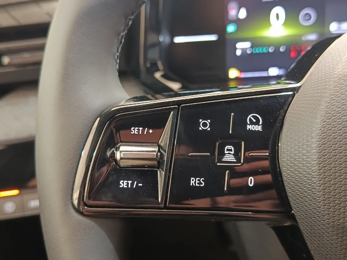 Gros plan sur les commandes multifonctions noires du volant réglable de la Renault Clio bleu, affichage numérique en arrière-plan.