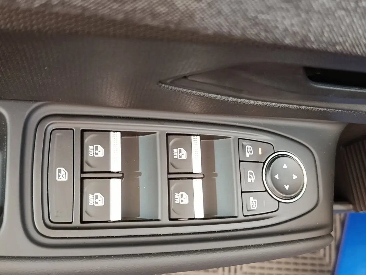 Gros plan sur les commandes des vitres électriques et rétroviseurs d'une Renault Clio bleu, côté conducteur.