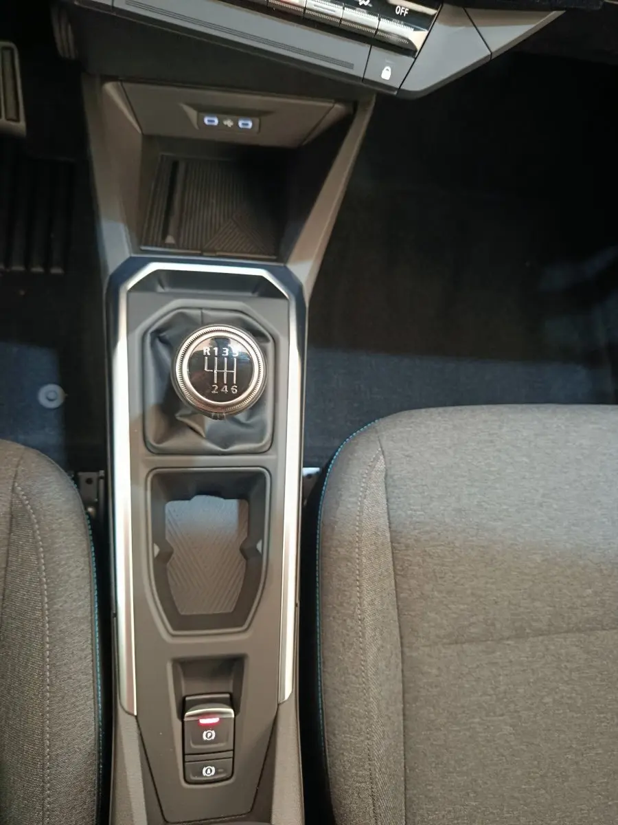 Vue plongeante sur la console centrale de la Renault Clio bleu, avec levier de vitesse manuel et frein à main électrique.