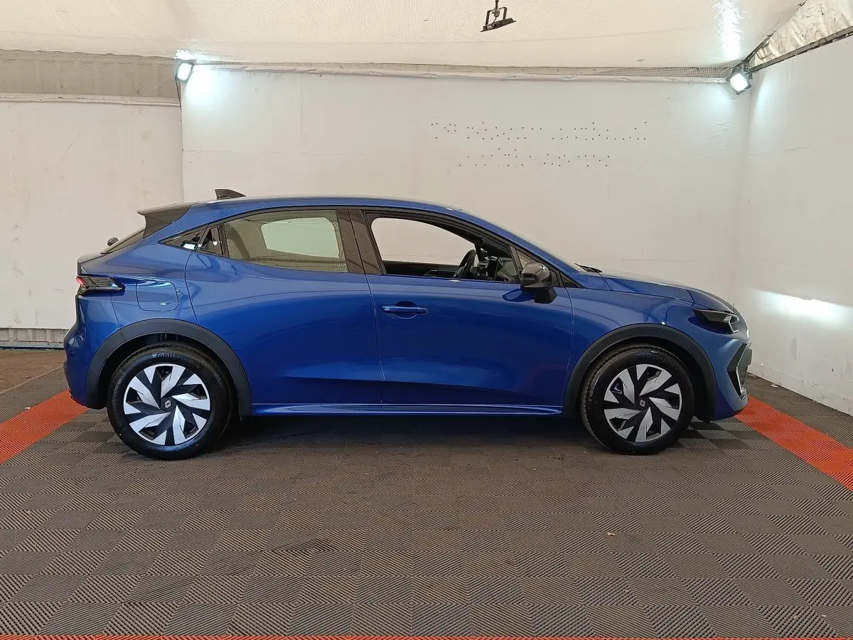 Profil droit d'une Renault Clio bleu 2026 avec jantes stylisées et toit noir dans un espace intérieur éclairé.