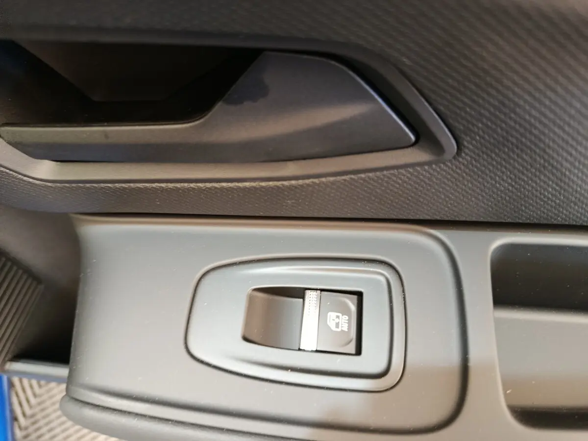 Gros plan sur le bouton de commande de la fenêtre électrique côté conducteur dans l’habitacle de la Renault Clio bleu.