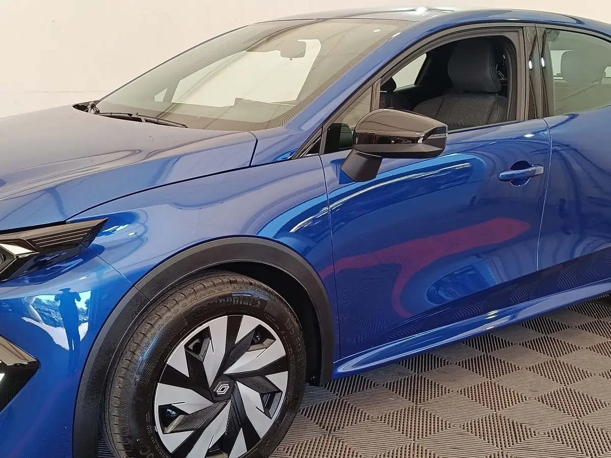 Vue de profil côté gauche d'une Renault Clio bleu métallisé avec jante au design géométrique et rétroviseur noir brillant.