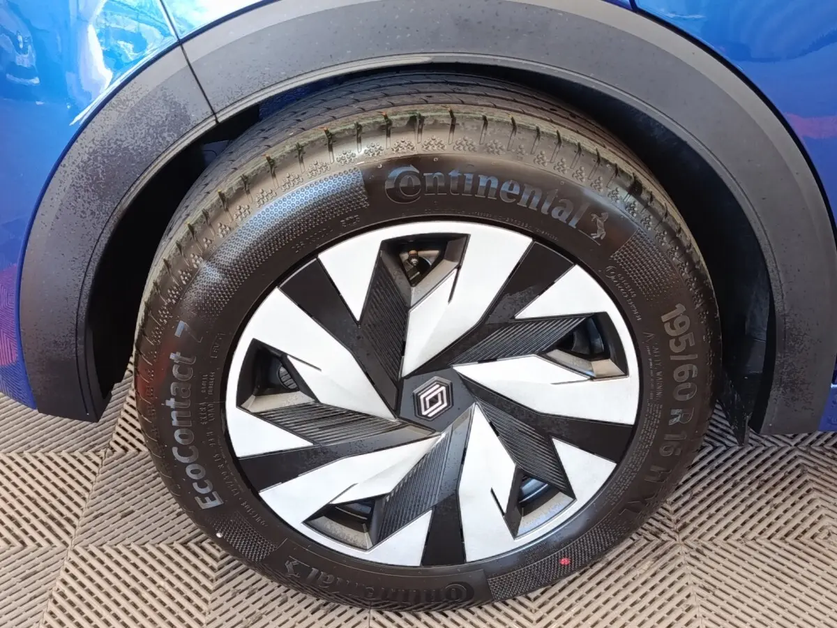 Gros plan sur la roue avant droite d’une Renault Clio bleue avec jante au design géométrique noir et argent.