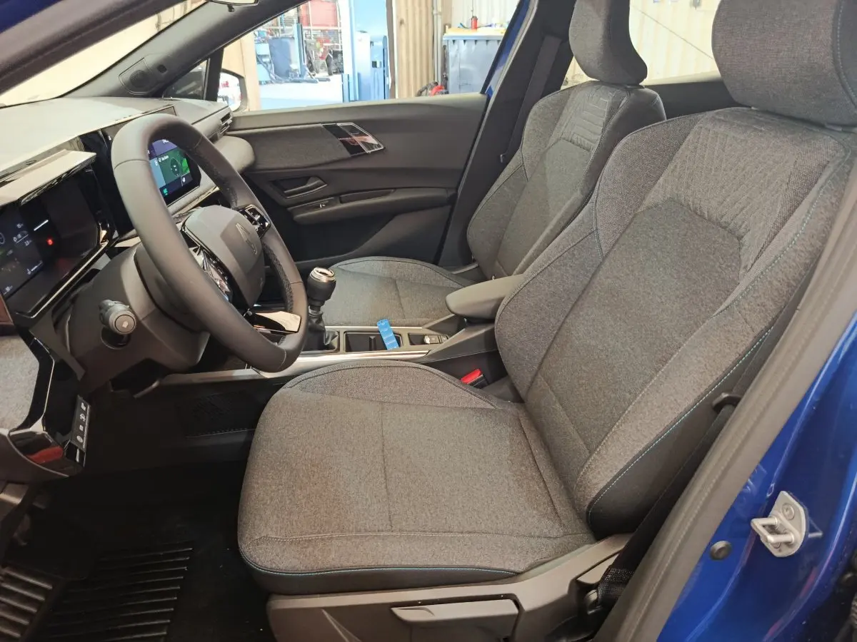 Intérieur côté conducteur de la Renault Clio bleu 2026, montrant sièges gris et volant multifonctions avec boîte manuelle.