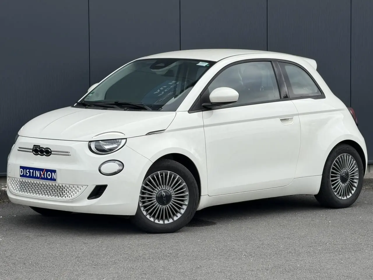 Fiat 500 électrique blanche vue 3/4 avant droit, avec jantes spécifiques et calandre sans grille.