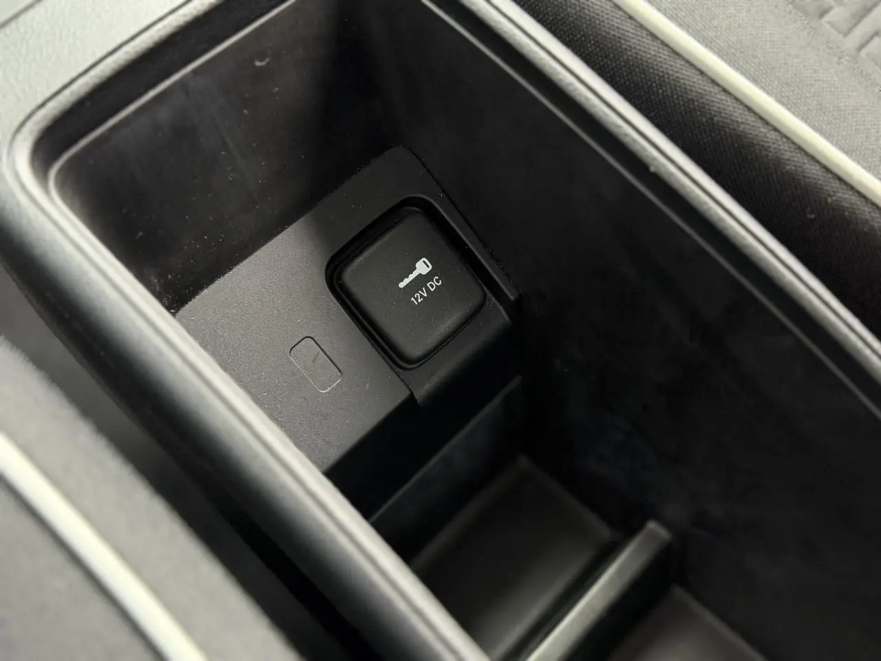Prise 12V dans le rangement central intérieur de la Fiat 500 électrique blanche, vue en plongée rapprochée.