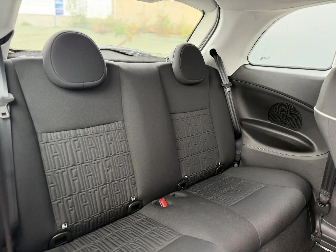 Vue intérieure arrière des sièges noirs avec motifs FIAT embossés sur la banquette d'une Fiat 500 électrique blanche.