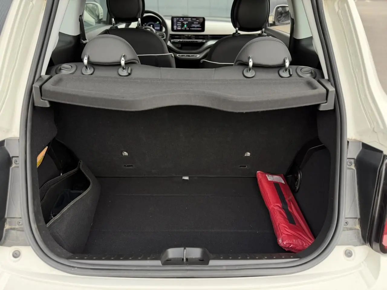 Coffre ouvert d'une FIAT 500 électrique blanche 2023, vue arrière montrant l'intérieur noir avec un kit de sécurité rouge.