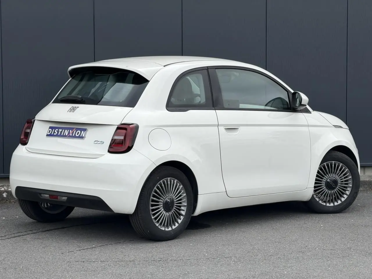 Fiat 500 électrique blanche vue 3/4 arrière droit, avec jantes stylisées et feux arrière foncés.