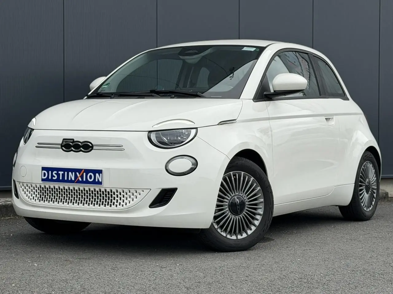 Fiat 500 électrique blanche vue 3/4 avant droit, avec jantes stylisées et calandre épurée.
