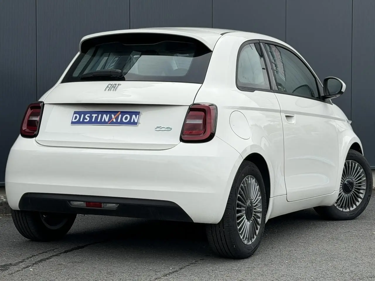 Vue 3/4 arrière droite d'une Fiat 500 électrique blanche avec feux arrière sombres et jantes stylisées.