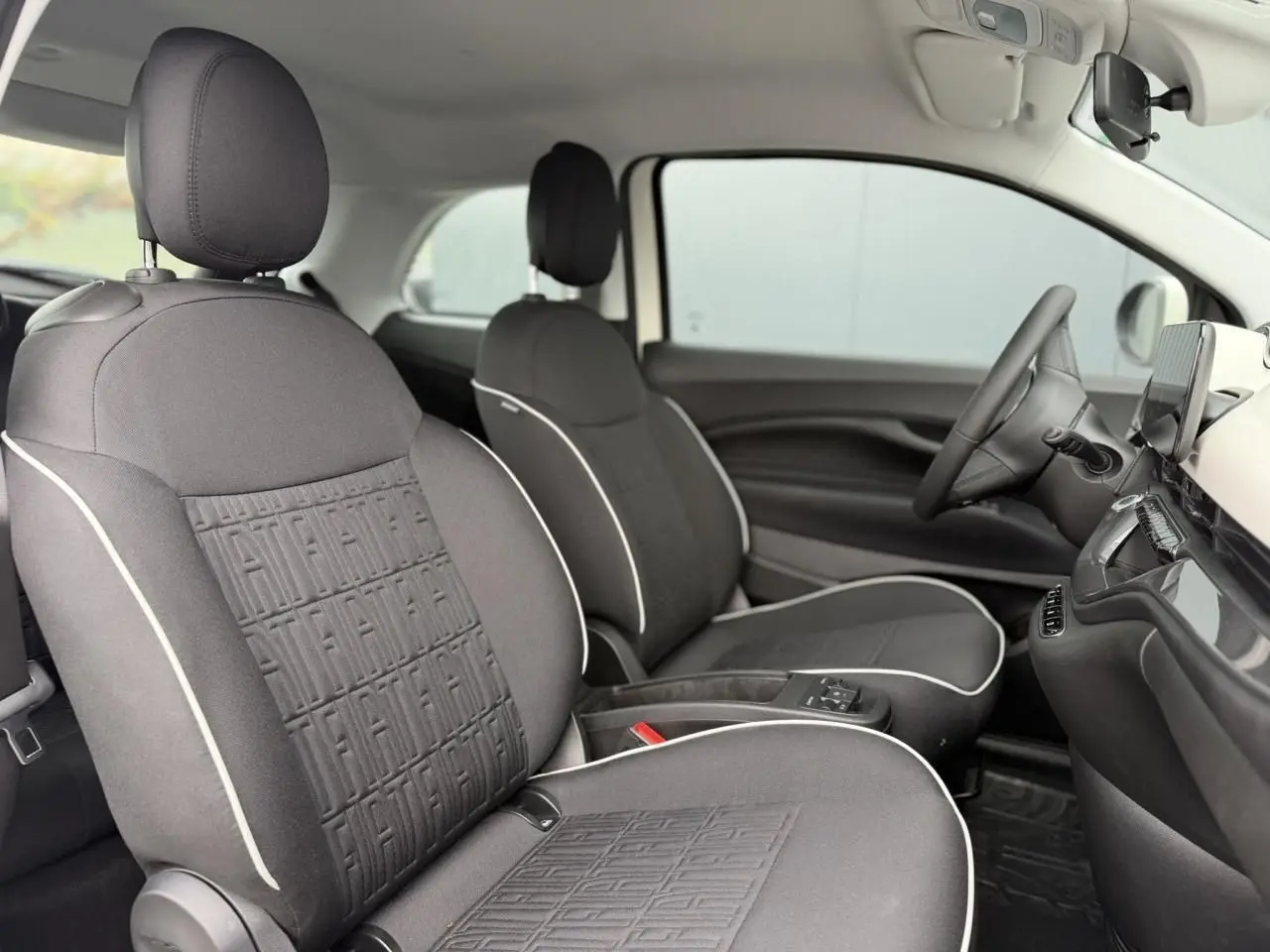 Vue intérieure côté gauche des sièges avant gris foncé avec surpiqûres blanches et motifs FIAT embossés sur une FIAT 500 électrique 2023.