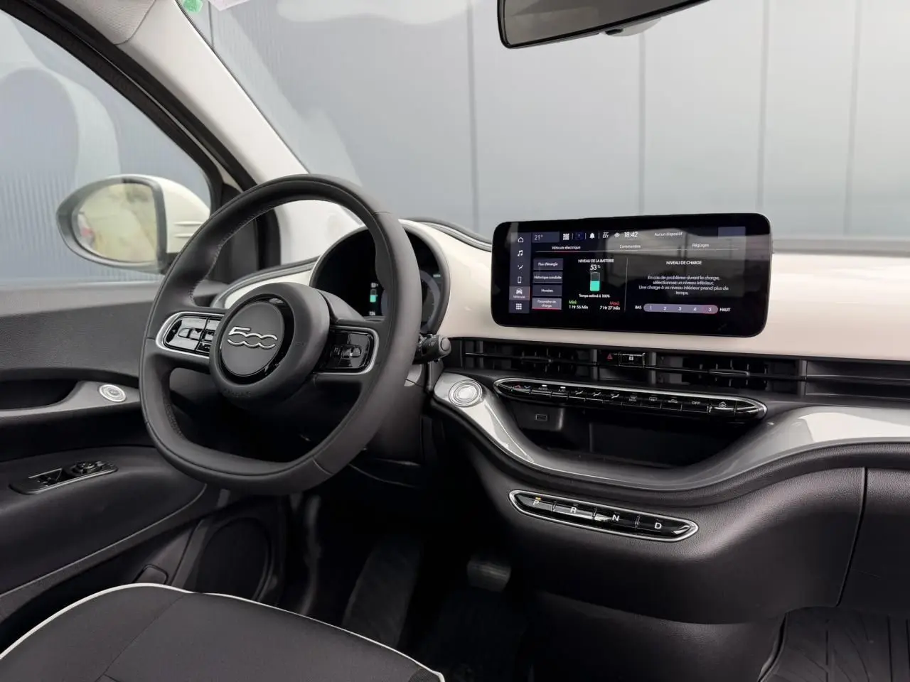Intérieur de la Fiat 500 électrique 2023, vue côté conducteur, tableau de bord blanc avec écran tactile central et volant noir.