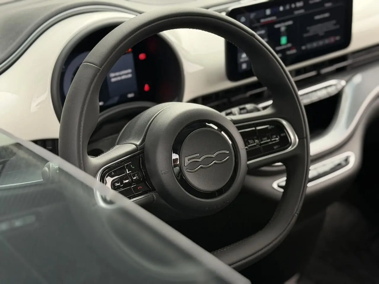 Vue rapprochée du volant noir et du tableau de bord blanc de la Fiat 500 électrique 2023 avec commandes intégrées.
