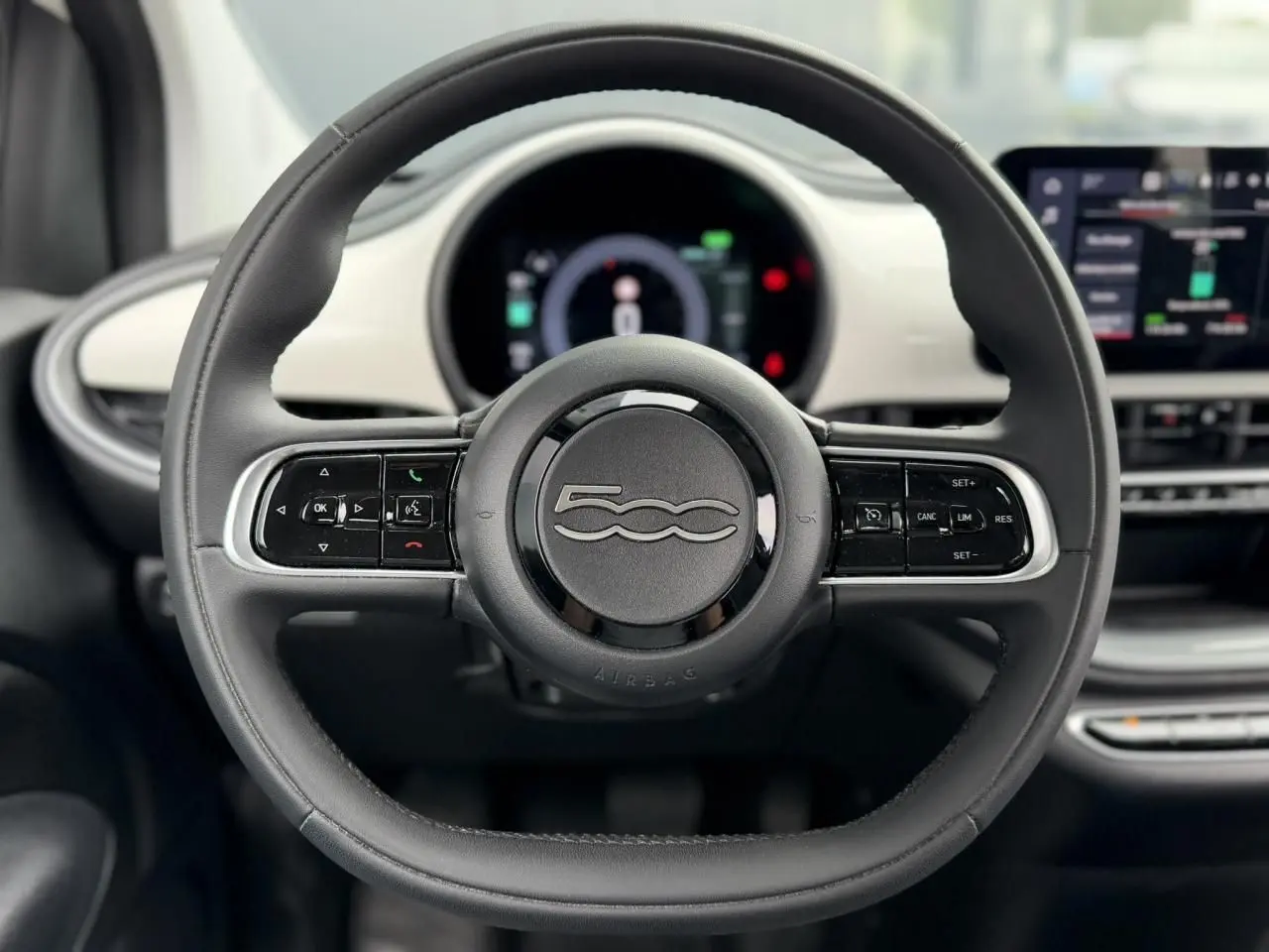Vue centrée sur le volant noir de la FIAT 500 électrique 2023 avec tableau de bord numérique et écran tactile.