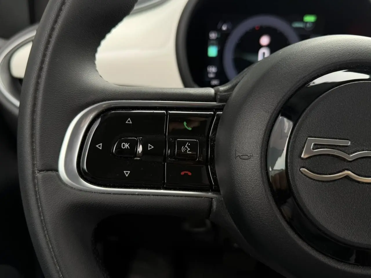 Gros plan sur le volant noir de la FIAT 500 électrique 2023 avec commandes intégrées et tableau de bord partiellement visible.