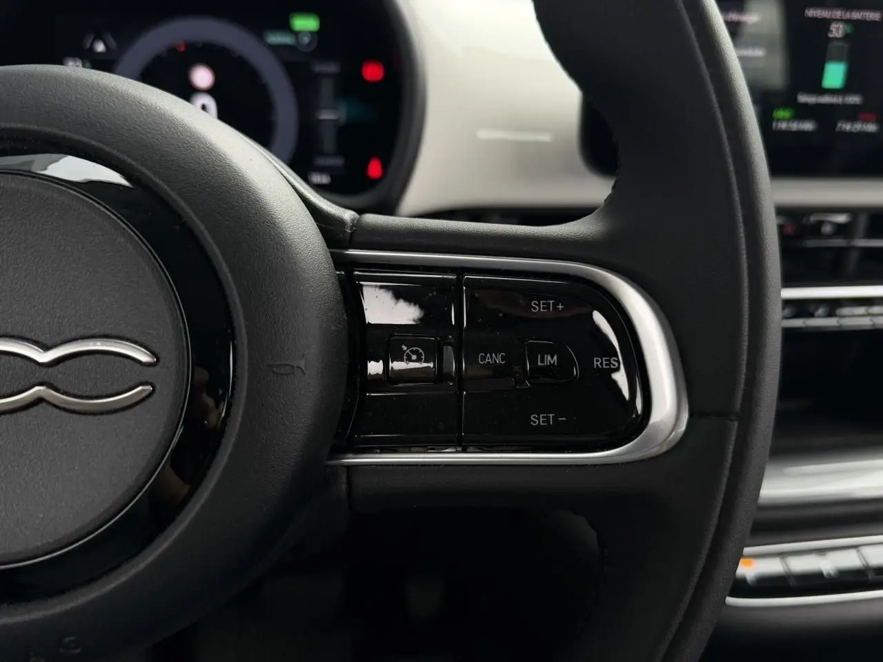 Gros plan sur le côté droit du volant noir de la FIAT 500 électrique blanche, avec commandes de régulateur de vitesse.