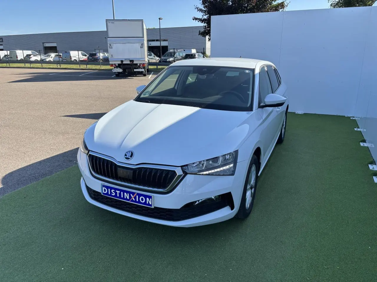 Vue 3/4 avant d'une Skoda Scala blanc glacier avec calandre noire et jantes alliage argent sur sol vert.