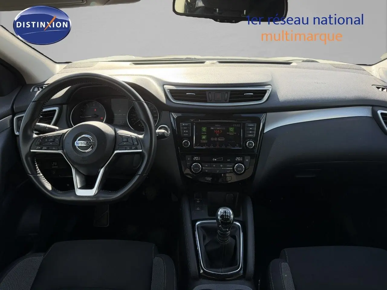 Vue intérieure frontale du tableau de bord et volant d'un Nissan Qashqai blanc nacré 2019 avec boîte manuelle.
