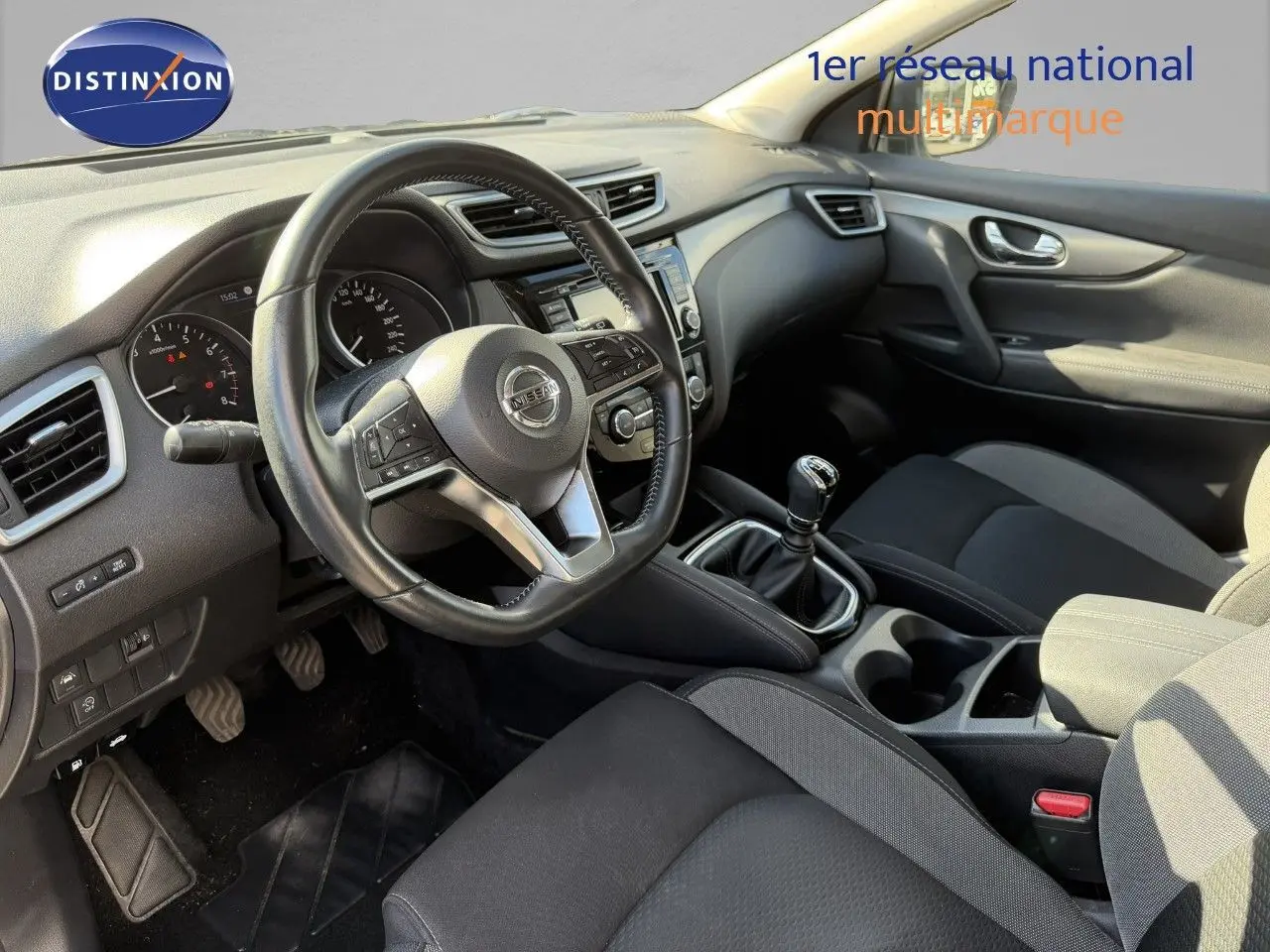 Vue intérieure côté conducteur du Nissan Qashqai blanc nacré 2019, avec volant multifonction et boîte manuelle.