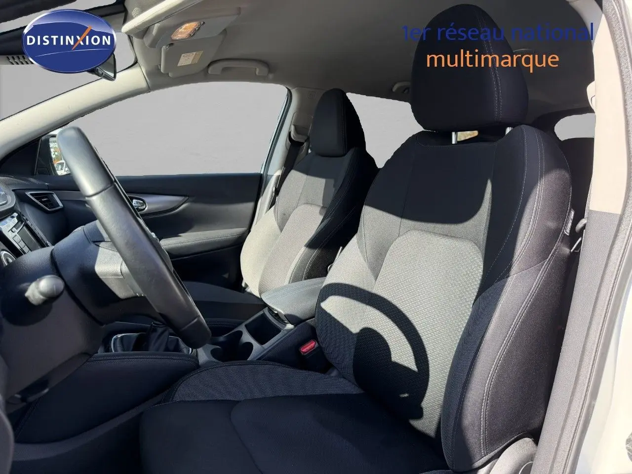 Vue intérieure côté conducteur du Nissan Qashqai blanc nacré, montrant les sièges avant en tissu noir et gris.