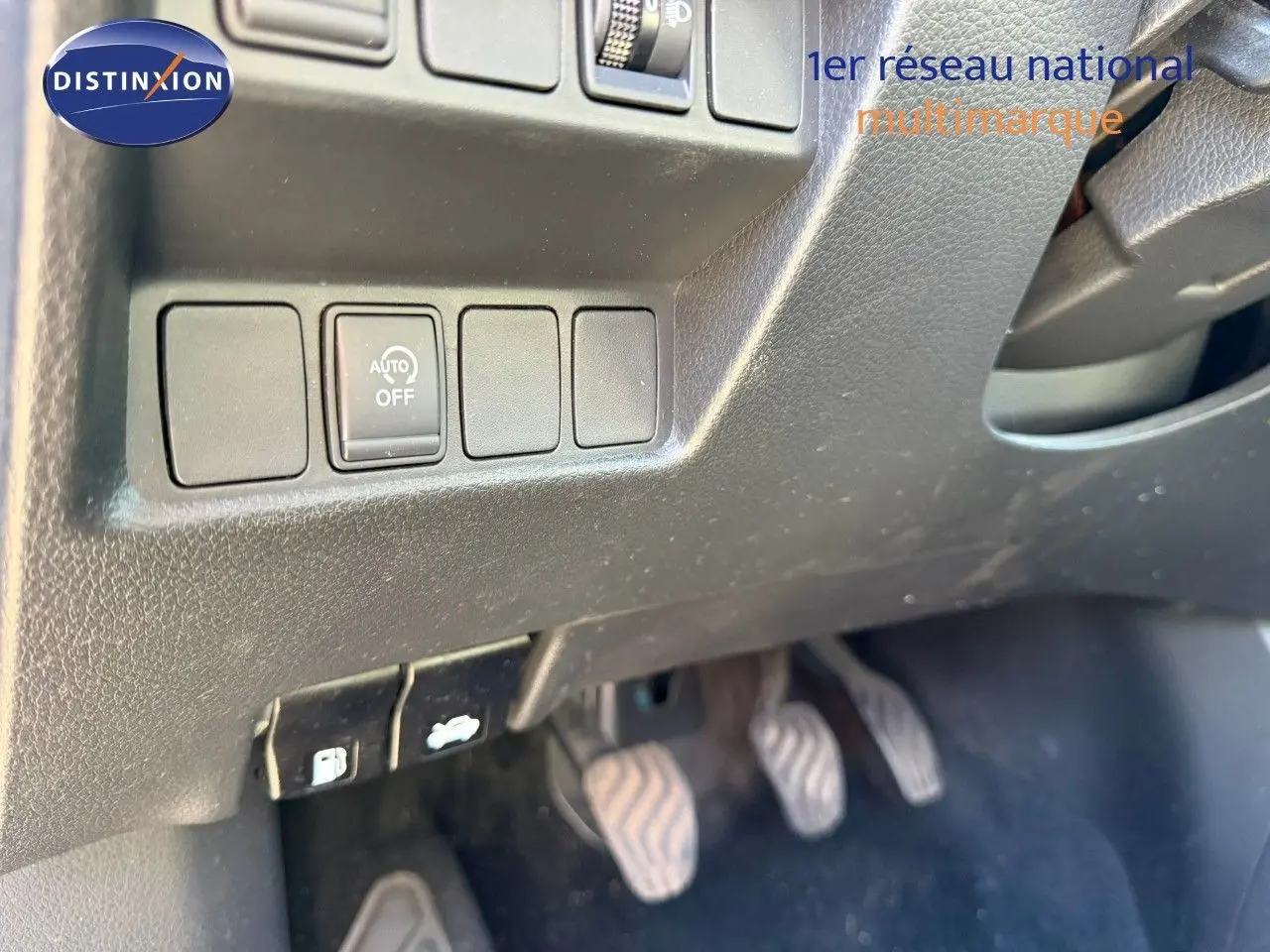 Gros plan sur les commandes sous le tableau de bord côté gauche d’un Nissan Qashqai blanc nacré, pédales visibles.