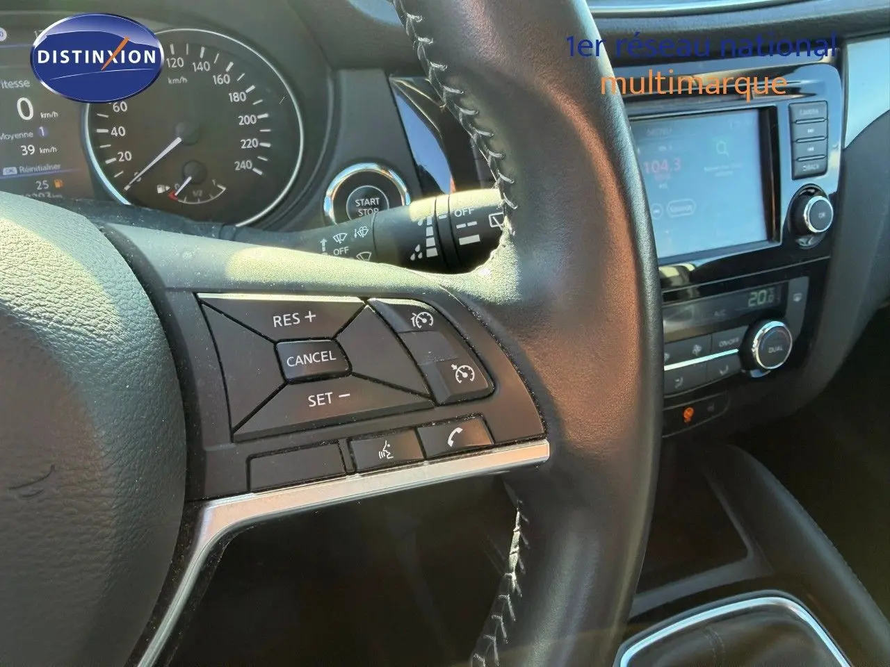 Gros plan sur le volant et le tableau de bord du Nissan Qashqai blanc nacré, avec commandes au volant et écran tactile visible.