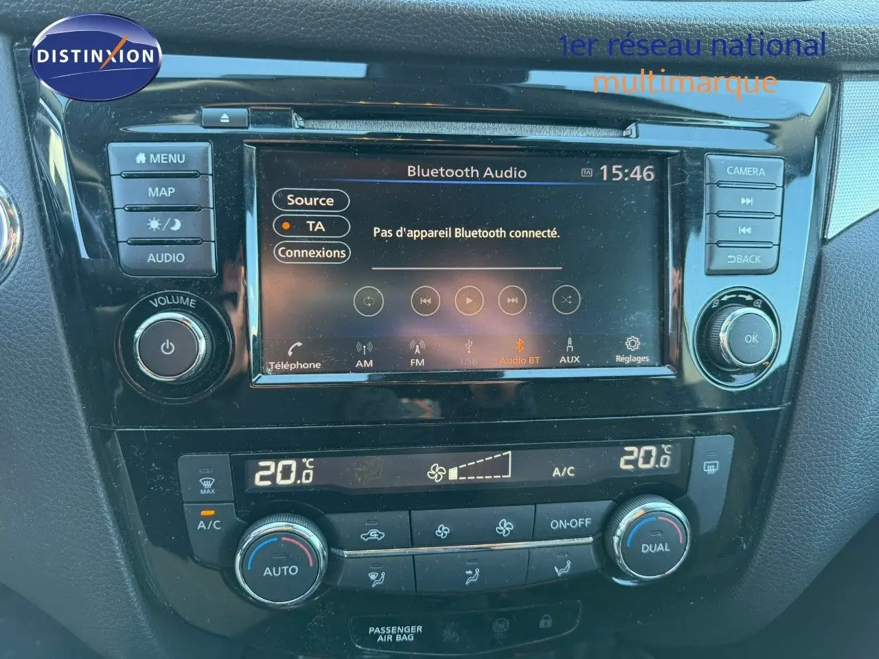 Tableau de bord de Nissan Qashqai blanc nacré, affichage central tactile avec options Bluetooth et climatisation réglée à 20°C.