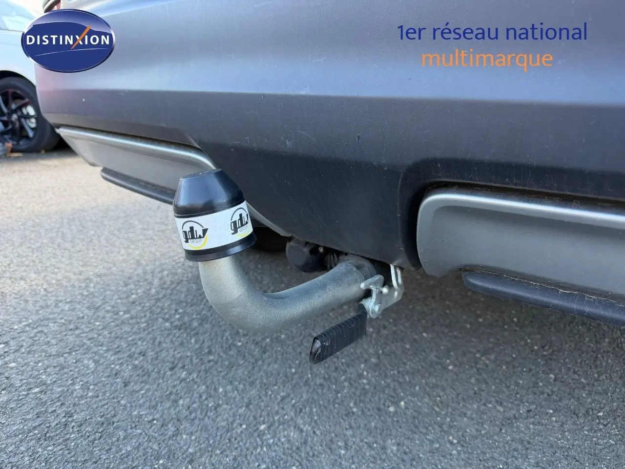 Gros plan sur l'attelage arrière d'un Nissan Qashqai blanc nacré, avec pare-chocs noir et sol goudronné visible.