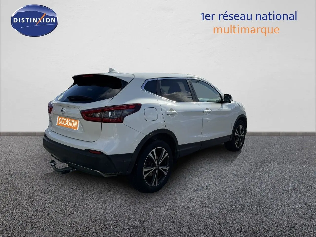 Vue 3/4 arrière droite d'un Nissan Qashqai blanc nacré avec jantes noires et attelage visible.