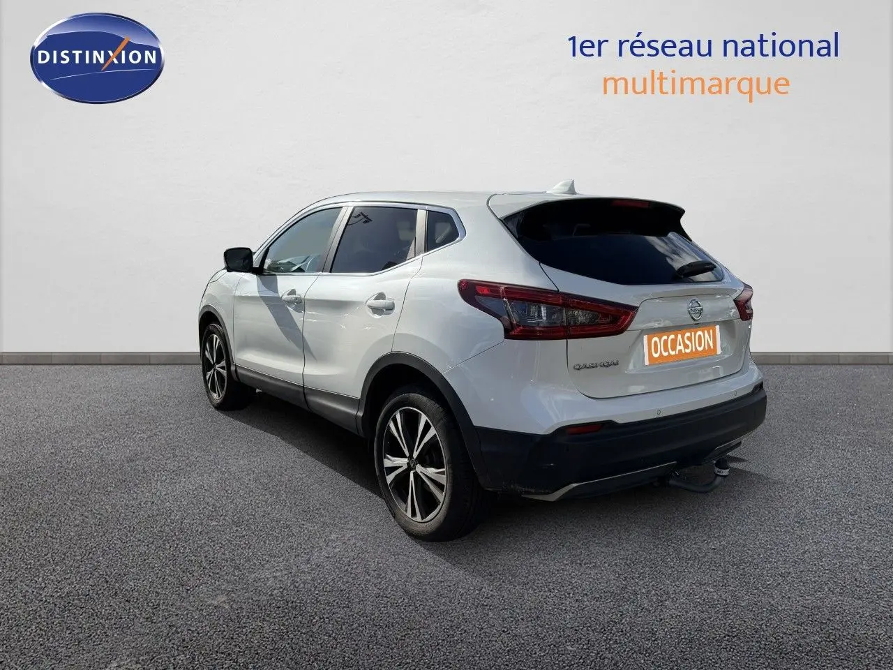 Vue 3/4 arrière droite du Nissan Qashqai blanc nacré avec jantes alliage et attelage visible sur fond neutre.