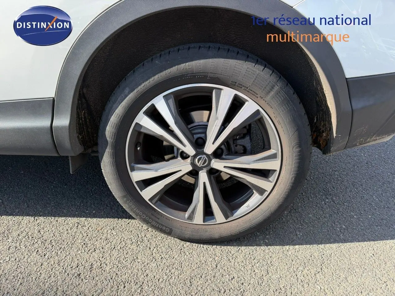 Gros plan sur la roue avant droite d’un Nissan Qashqai blanc nacré avec jante alliage à design moderne.