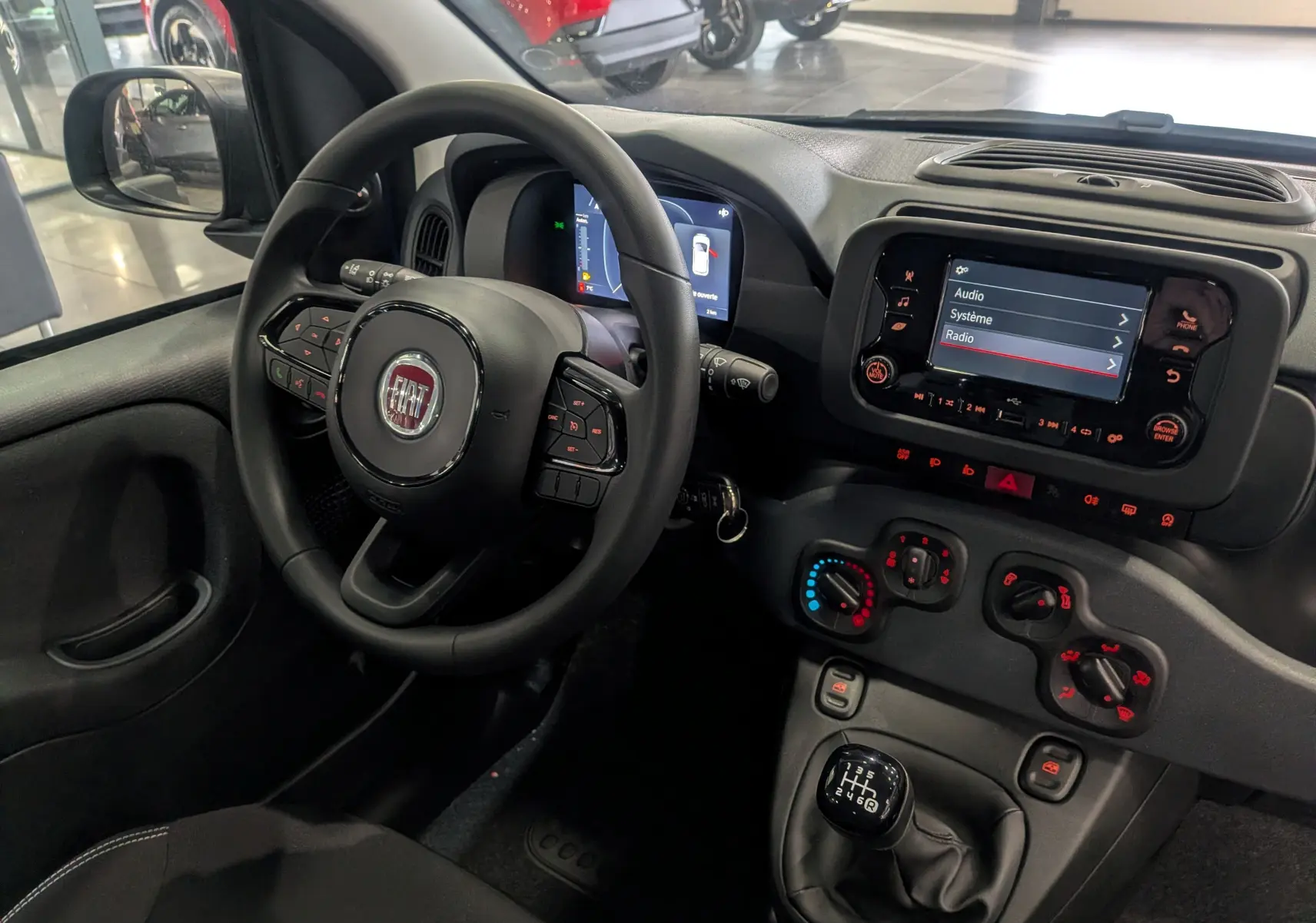 Intérieur de la Fiat Panda 1.0 Hybrid 2025 vu côté conducteur, tableau de bord avec écran tactile et commandes manuelles.