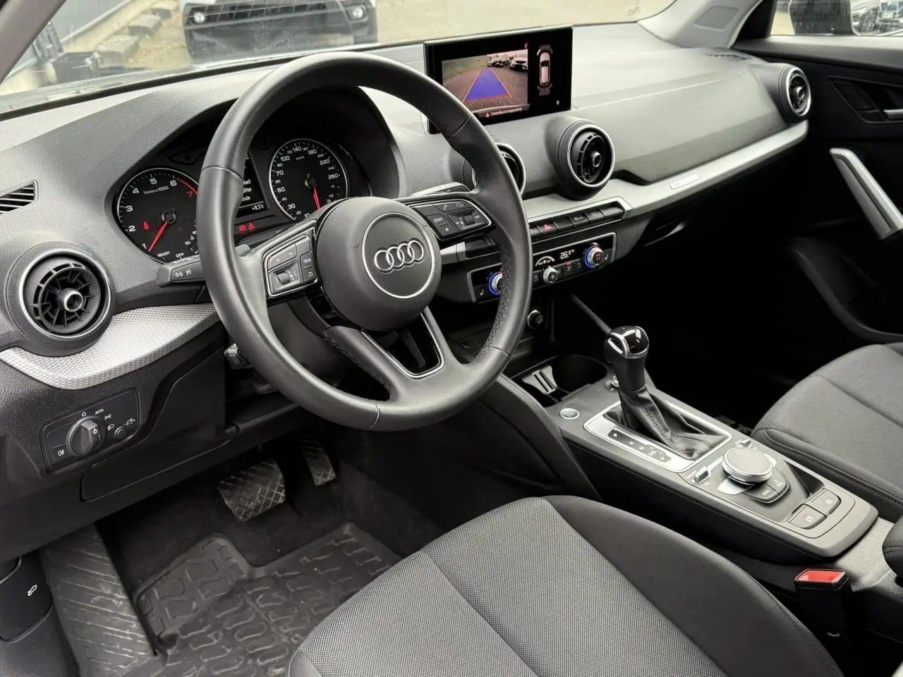 Intérieur avant droit de l'Audi Q2 35 TFSI 2023 avec tableau de bord noir, écran caméra de recul et console centrale automatique.