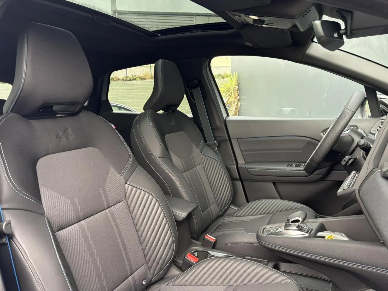 Vue intérieure côté conducteur du Renault Captur Esprit Alpine 2025, sièges noirs avec logo Alpine et toit ouvrant électrique.