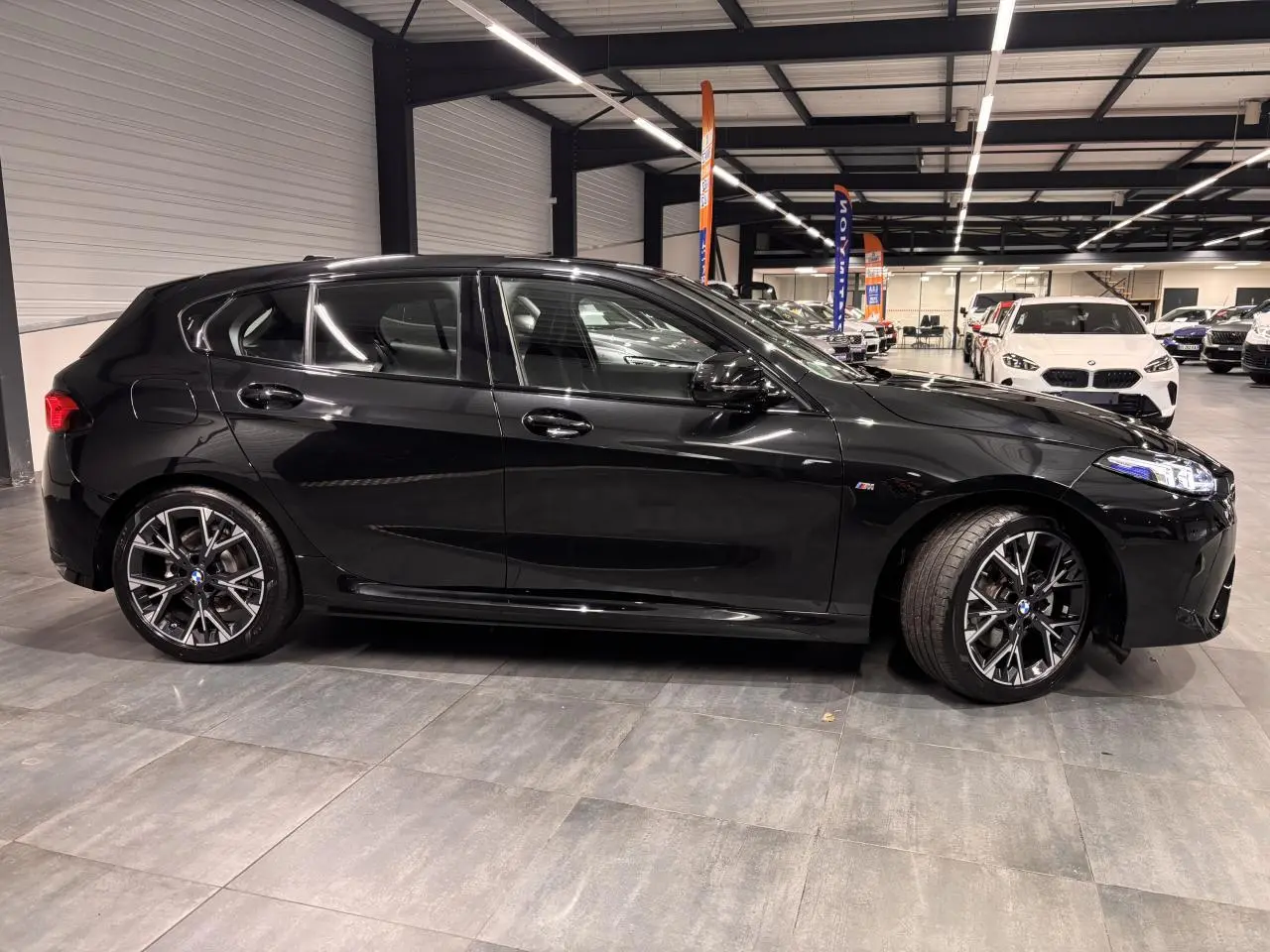 BMW Série 1 118d M Sport noir métal vue de profil côté gauche avec jantes alliage 18 pouces en intérieur showroom.