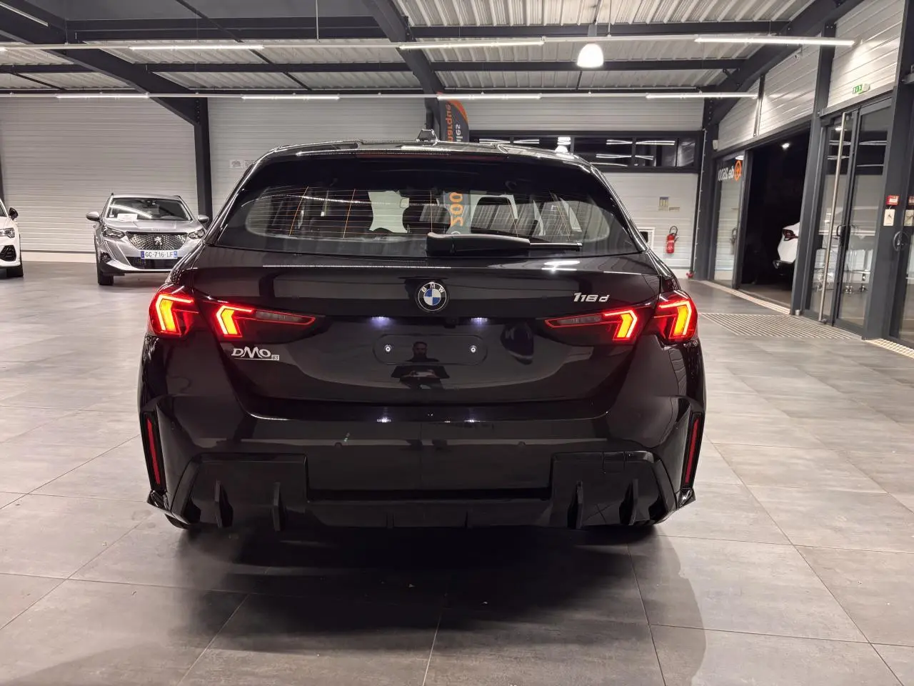 Vue arrière d'une BMW Série 1 118d noire métal avec feux arrière LED allumés dans un showroom.