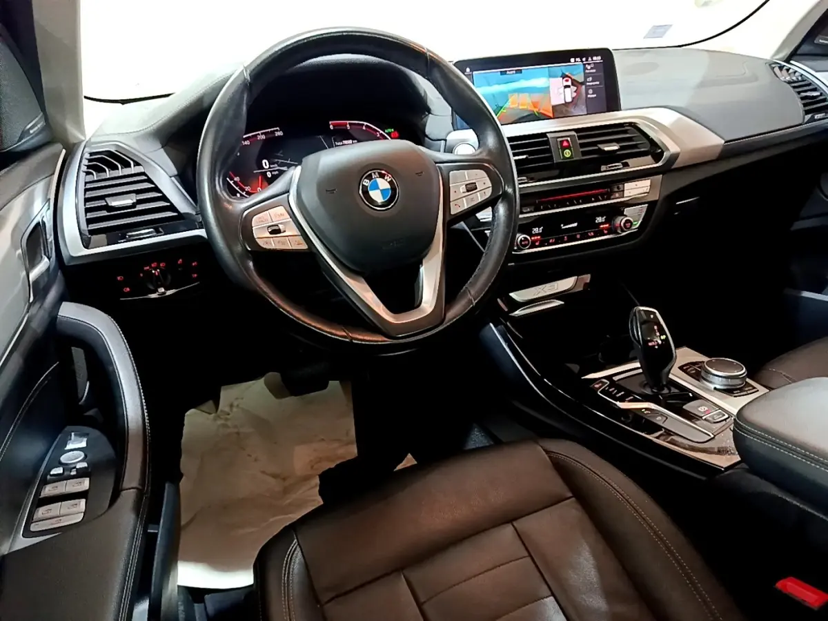Vue intérieure côté conducteur du BMW X3 noir 2019, volant cuir, écran tactile central et console moderne.