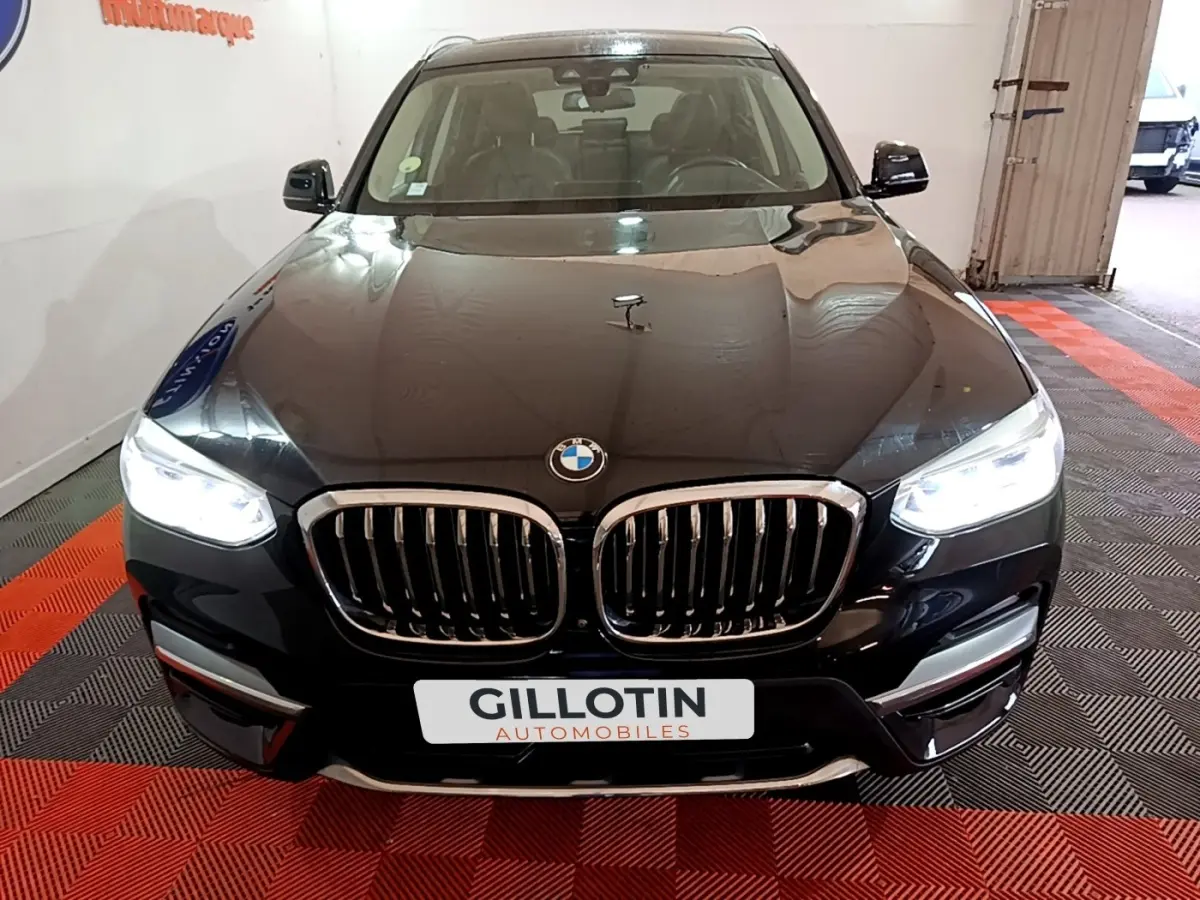 Vue avant d'un BMW X3 sDrive18d noir avec calandre double haricot et phares LED allumés en intérieur showroom.