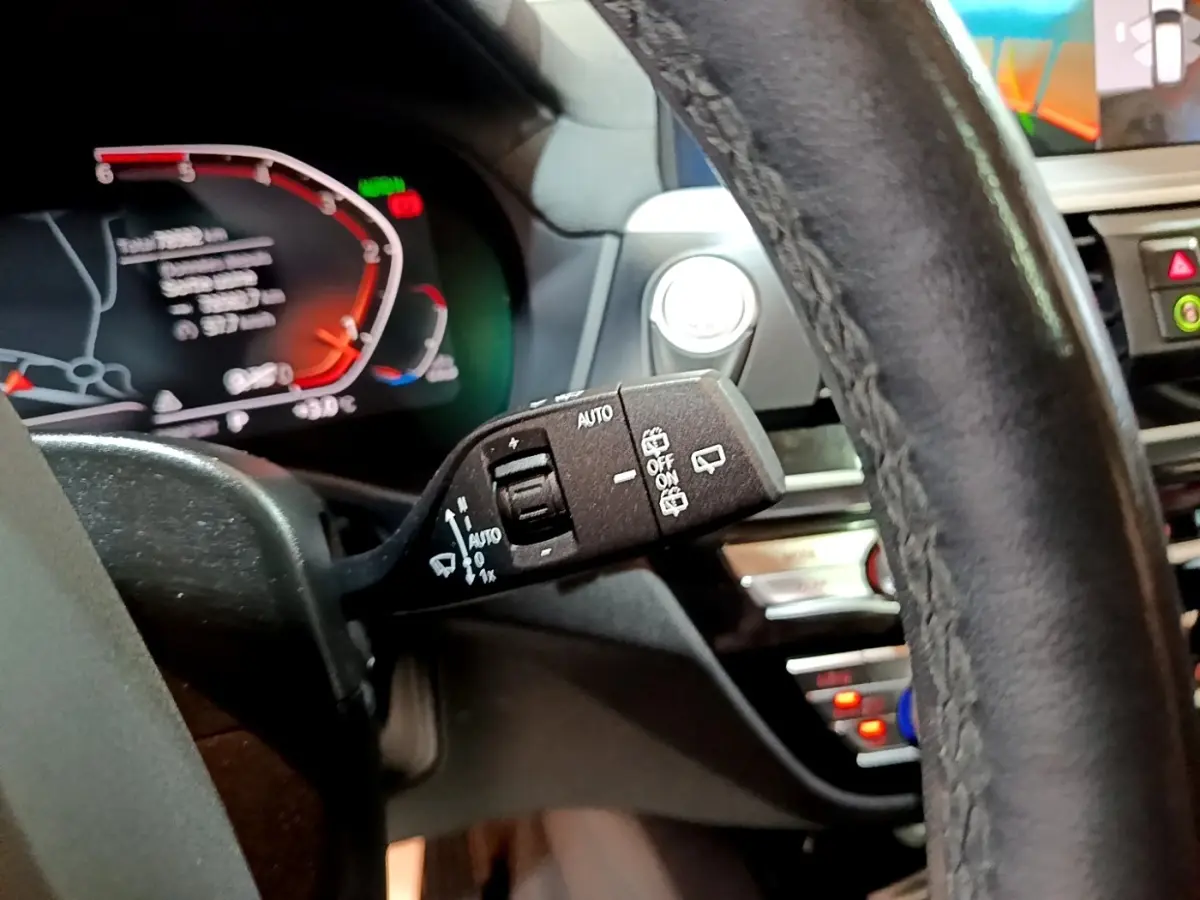 Gros plan sur la manette de commande des essuie-glaces à gauche du volant cuir noir du BMW X3 sDrive18d 2019, tableau de bord numérique visible.