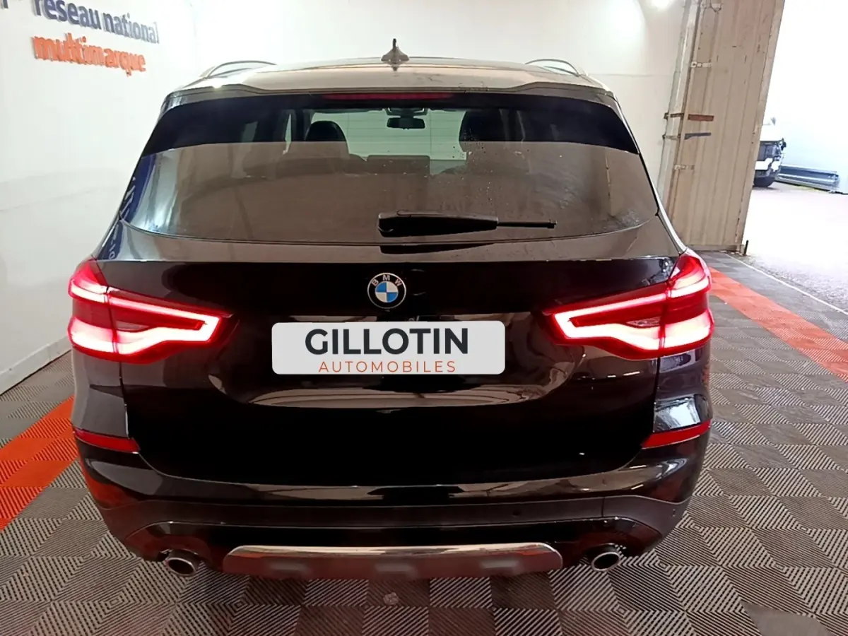 Vue arrière d'un BMW X3 noir avec feux arrière allumés dans un garage intérieur.