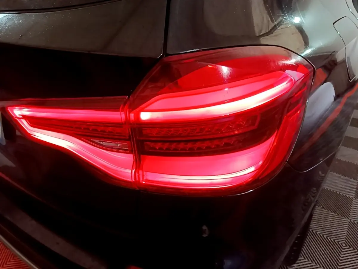 Gros plan sur le feu arrière droit allumé d’un BMW X3 noir, soulignant les lignes lumineuses LED distinctives.